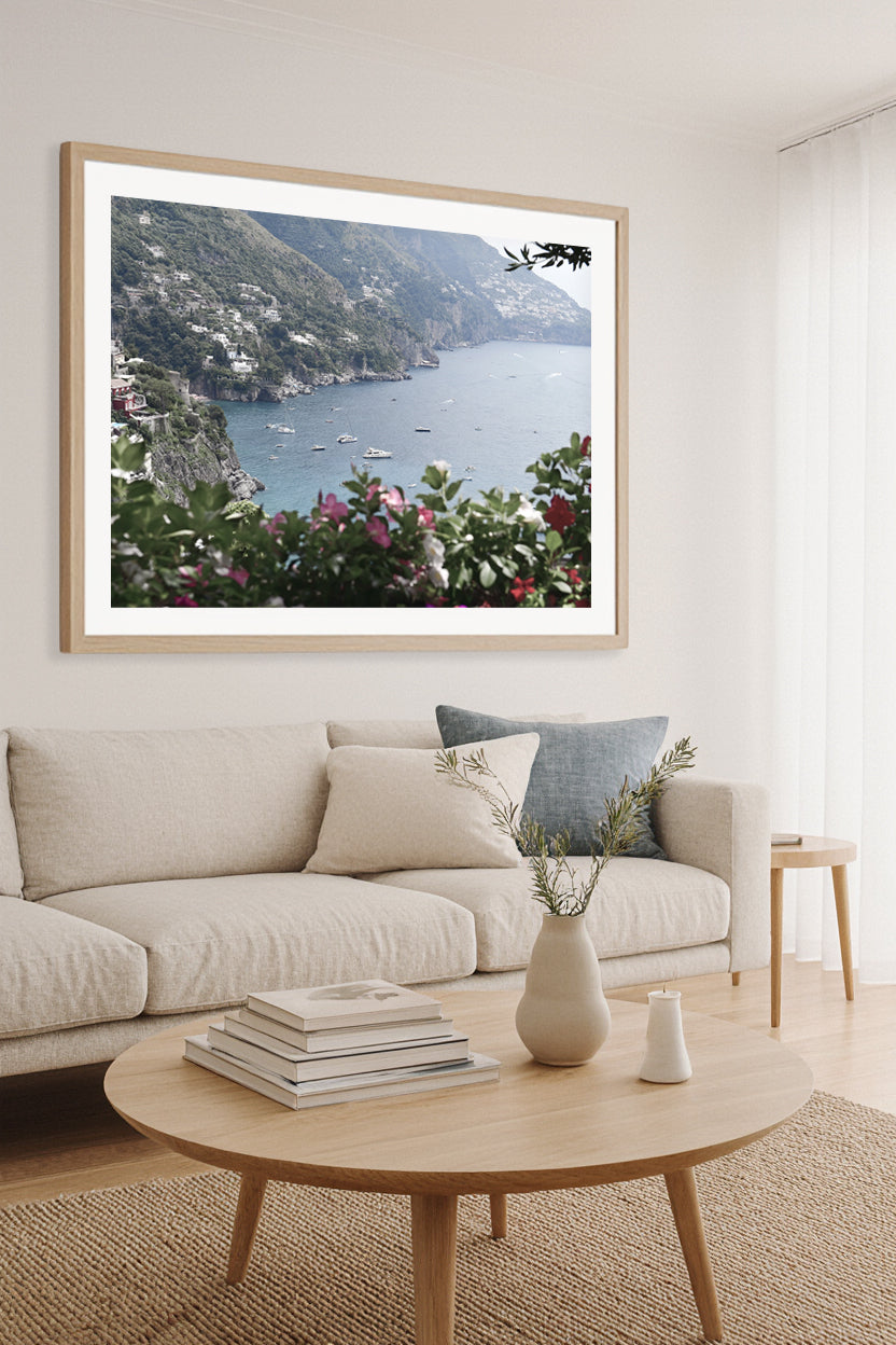 Fine art photography of the Amalfi Coast with boats and cliffs, framed wall art print above a neutral sofa in a coastal-inspired living room.