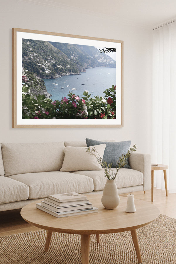 Fine art photography of the Amalfi Coast with boats and cliffs, framed wall art print above a neutral sofa in a coastal-inspired living room.