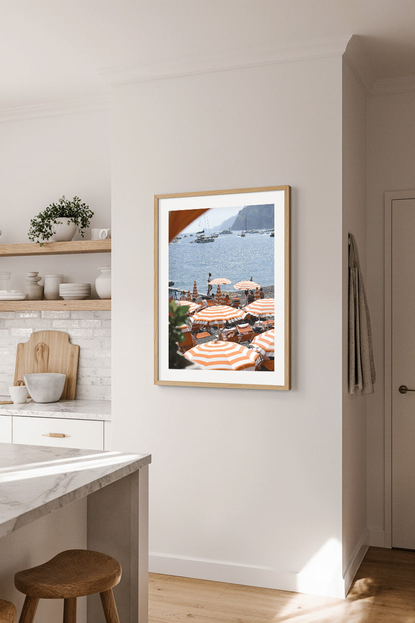 Framed travel print of a Arienzo Beach Club with orange umbrellas in a modern kitchen.