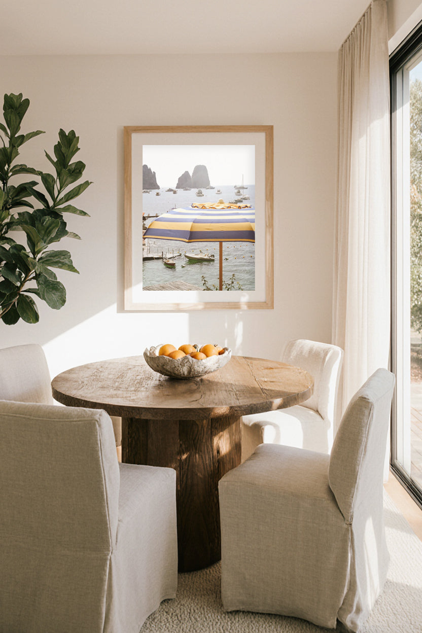 Capri travel photography print featuring a striped yellow umbrella, Faraglioni rocks, and serene sea views, elegant coastal wall art for home décor.