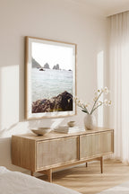 Framed wall art print of Capri’s Faraglioni sea stacks, styled in a coastal bedroom above a natural wood console with orchids.