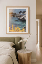 Framed artwork of a coastal scene above a bed in a modern bedroom. Coastal travel photography bringing Italian summers to home décor.