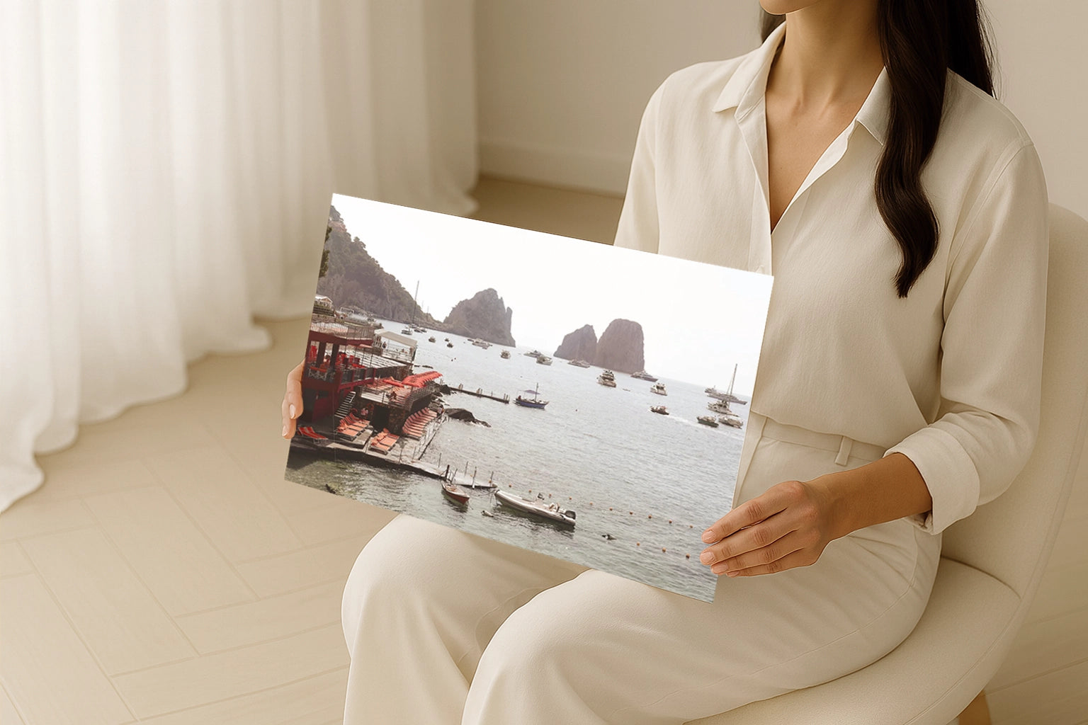 Woman holding a travel photography wall art print of Capri, Italy featuring a beach club, boats, and Faraglioni rock formations.