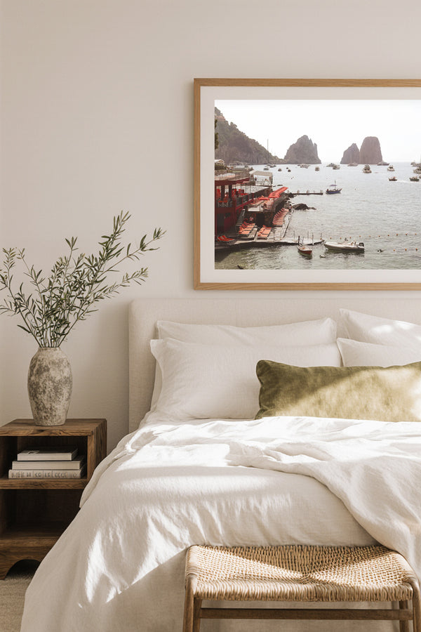 Framed wall art of Capri’s iconic beach club with red sun loungers and Faraglioni rocks, styled above a bed in a serene coastal-inspired bedroom.
