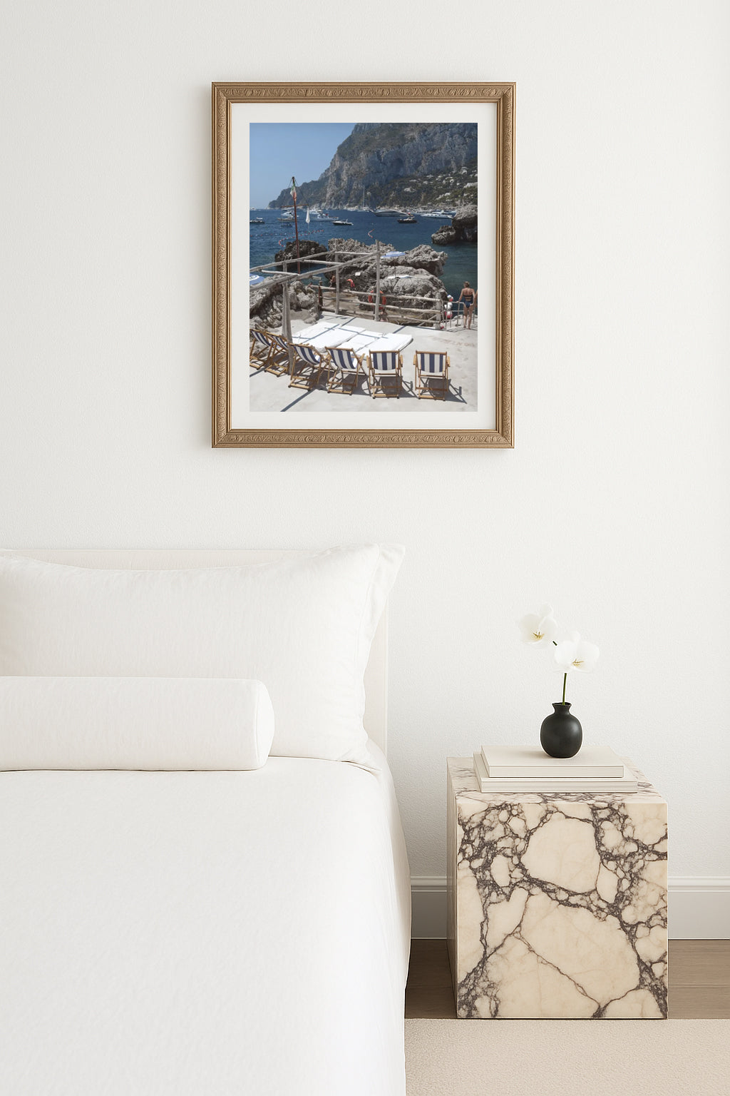 Framed coastal artwork of a La Fontelina Beach Club in Capri styled  above a bed in a bedroom.