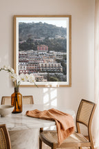 Framed art print of Positano town and colorful Mediterranean architecture, styled as wall art in a modern dining space.