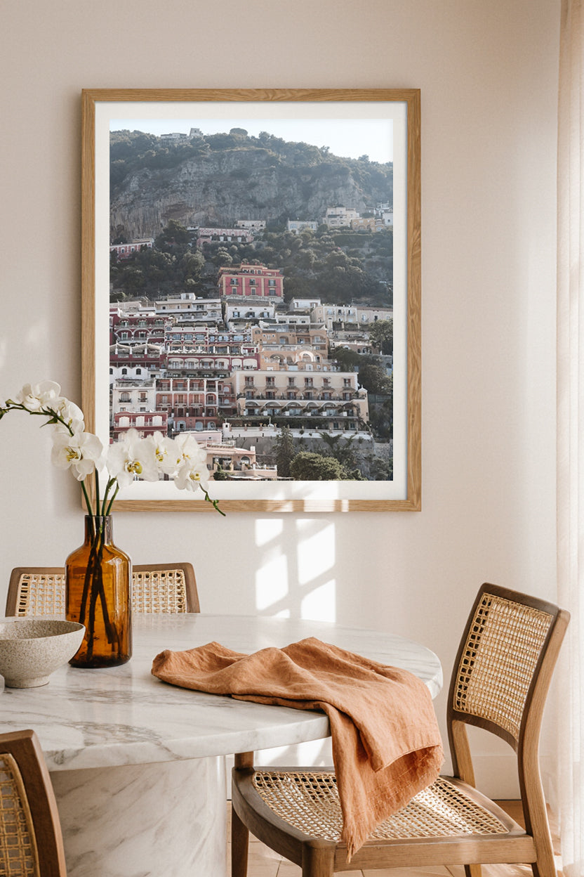 Framed art print of Positano town and colorful Mediterranean architecture, styled as wall art in a modern dining space.
