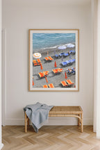 Fine art photography print of Positano beach club in Italy, featuring vibrant orange sunbeds and blue striped umbrellas along the shoreline, coastal Mediterranean wall art décor.